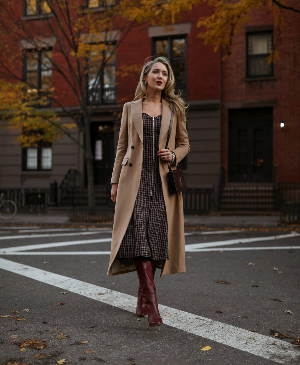 NYC style blogger in plaid midi dress, tall boots and long camel coat in New York sidewalk in fall season